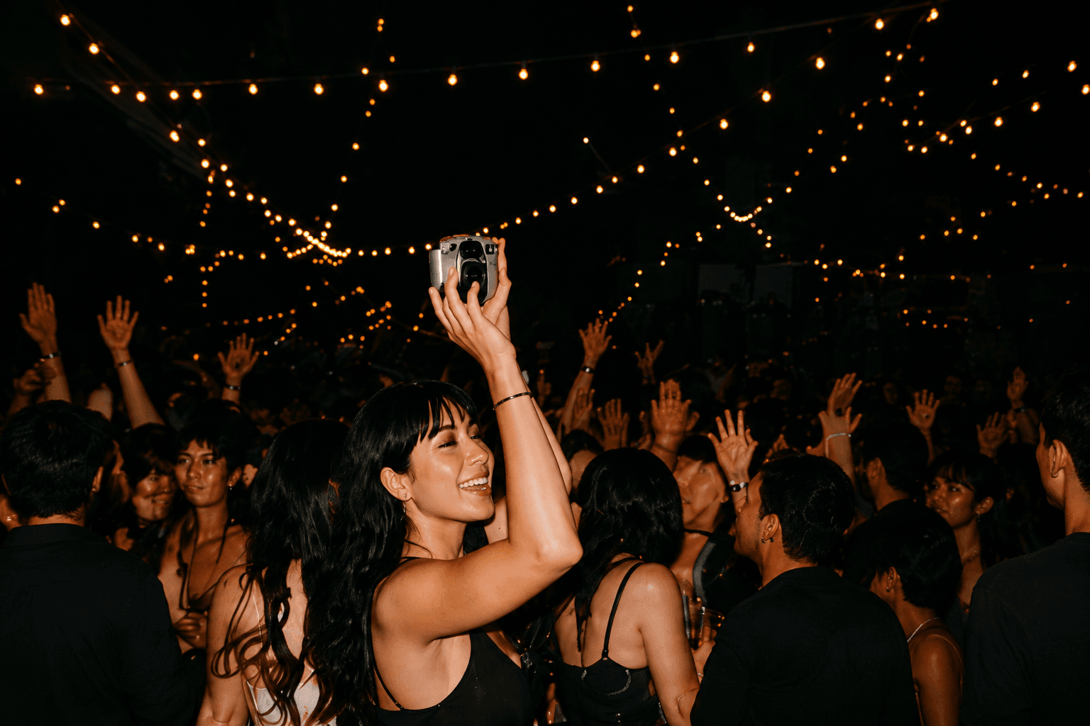 Crowded dance floor beneath string lights with a camera held overhead