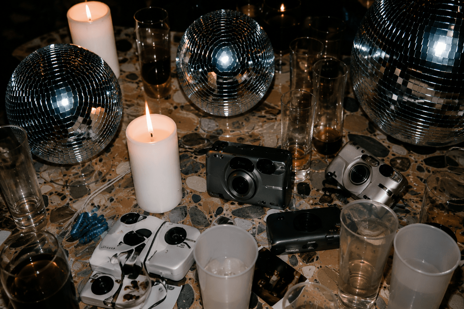 Compact cameras, candles, glasses, and mirrored disco balls on a party table